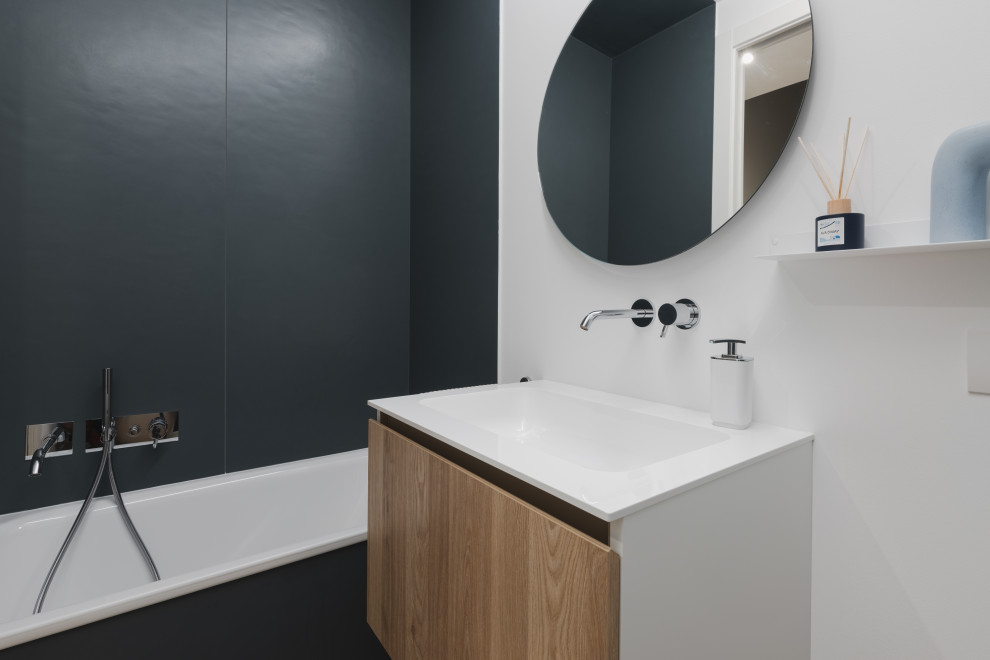 Inspiration for a small scandi bathroom in Milan with flat-panel cabinets, light wood cabinets, an alcove bath, a two-piece toilet, blue tiles, porcelain tiles, white walls, light hardwood flooring, an integrated sink, solid surface worktops, beige floors, white worktops, a wall niche, a single sink and a floating vanity unit.