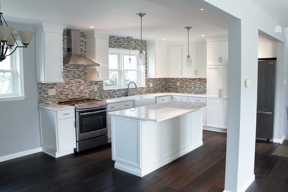 Mid-sized transitional l-shaped eat-in kitchen in Philadelphia with a farmhouse sink, shaker cabinets, white cabinets, quartz benchtops, blue splashback, mosaic tile splashback, stainless steel appliances, vinyl floors, with island and brown floor.