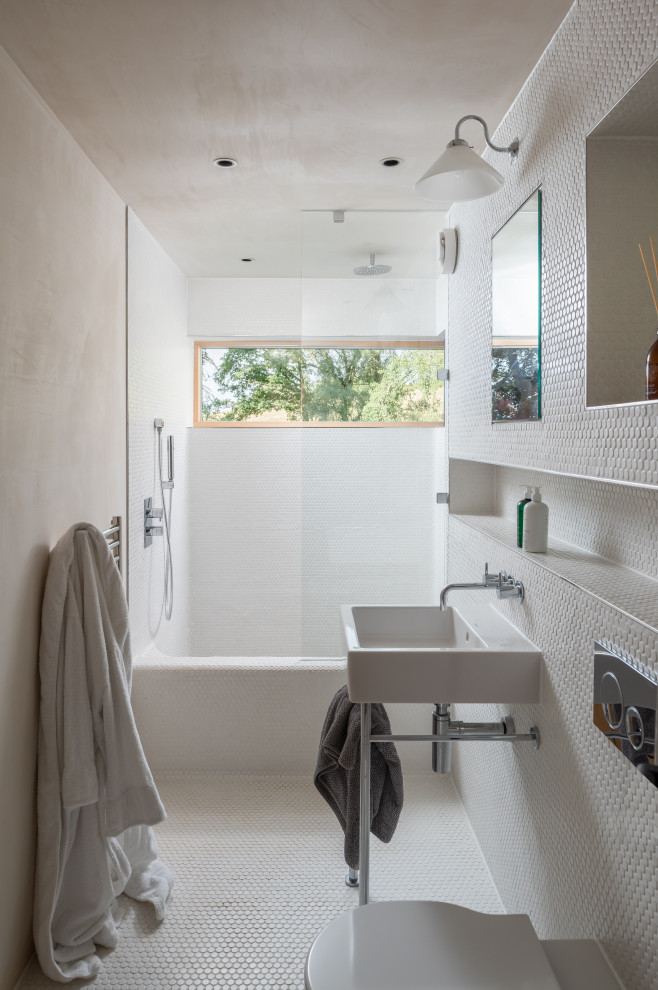 This is an example of a mid-sized country kids bathroom in Devon with a curbless shower, a wall-mount toilet, white tile, pebble tile, white walls, pebble tile floors, a wall-mount sink, tile benchtops, white floor, a hinged shower door, white benchtops, a single vanity and a floating vanity.