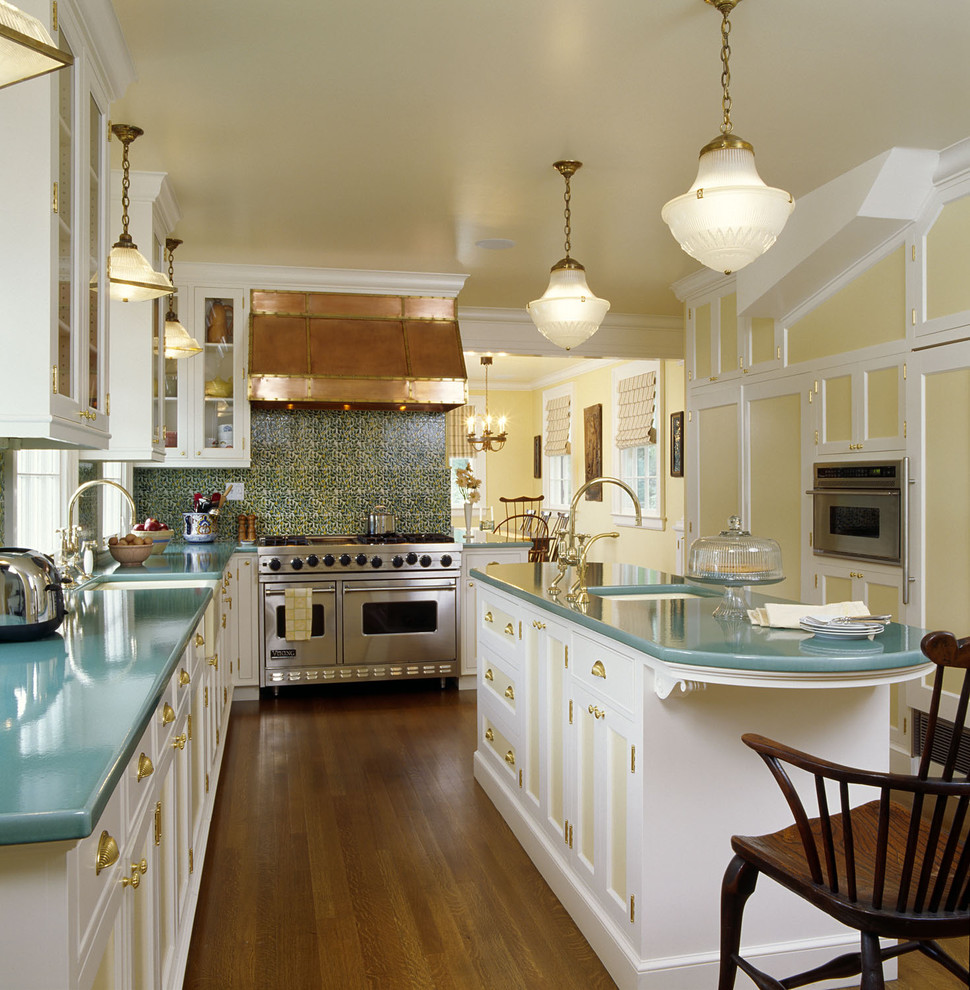 Photo of a mid-sized traditional l-shaped separate kitchen in Santa Barbara with a farmhouse sink, recessed-panel cabinets, white cabinets, green splashback, panelled appliances, with island, ceramic splashback, medium hardwood floors and turquoise benchtop.