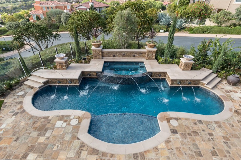 Large transitional backyard custom-shaped pool in Orange County with natural stone pavers.