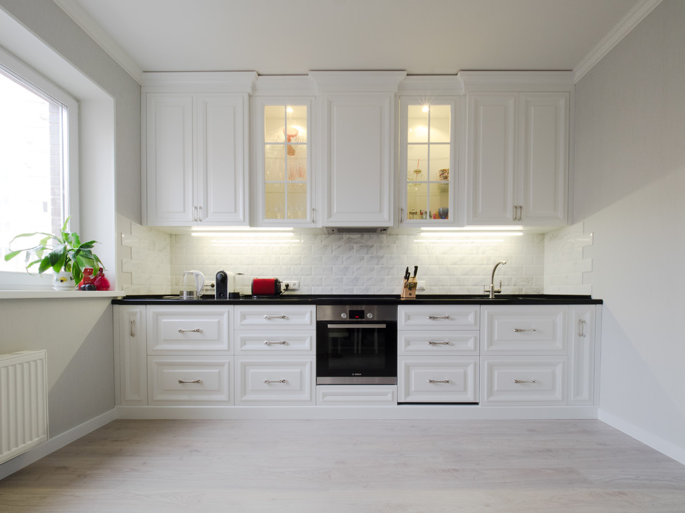 This is an example of a mid-sized transitional single-wall eat-in kitchen in Moscow with an undermount sink, white cabinets, solid surface benchtops, stainless steel appliances, laminate floors, no island, beige floor, raised-panel cabinets and white splashback.