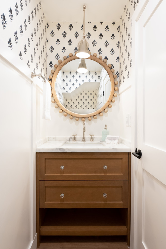 Small traditional powder room in San Francisco with shaker cabinets, brown cabinets, a one-piece toilet, white walls, medium hardwood floors, an undermount sink, marble benchtops, brown floor, white benchtops, a built-in vanity and wallpaper.
