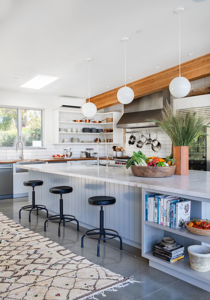 Contemporary l-shaped eat-in kitchen in Los Angeles with a farmhouse sink, white splashback, subway tile splashback, stainless steel appliances, with island, grey floor, white benchtop and concrete floors.