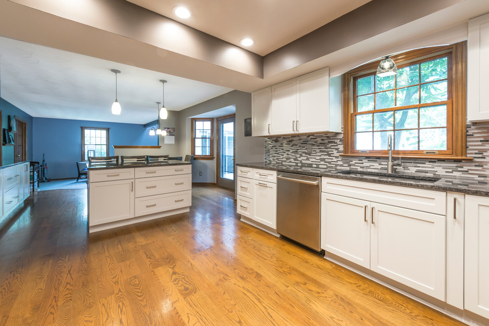 This is an example of a modern eat-in kitchen in Columbus with granite benchtops, grey splashback, stainless steel appliances and medium hardwood floors.