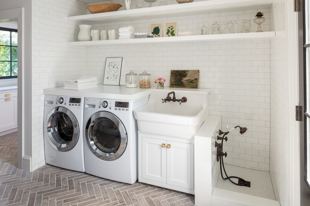 This is an example of a country single-wall utility room in Boston with a farmhouse sink, open cabinets, white cabinets, white walls, brick floors, a side-by-side washer and dryer and white benchtop.