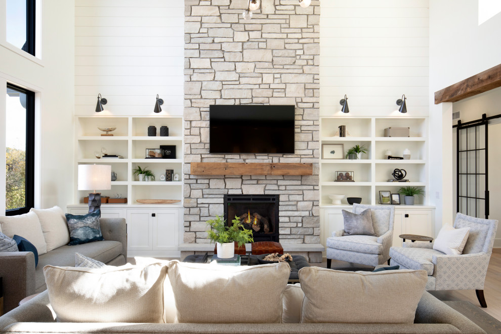 Design ideas for an expansive transitional open concept living room in Minneapolis with white walls, light hardwood floors, a standard fireplace, a stone fireplace surround, a built-in media wall, beige floor, vaulted and planked wall panelling.