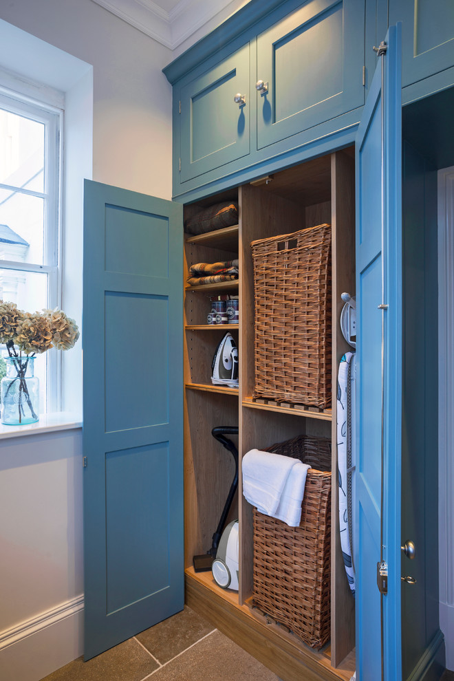 Mid-sized transitional laundry room in Hampshire with blue cabinets, limestone floors and shaker cabinets.