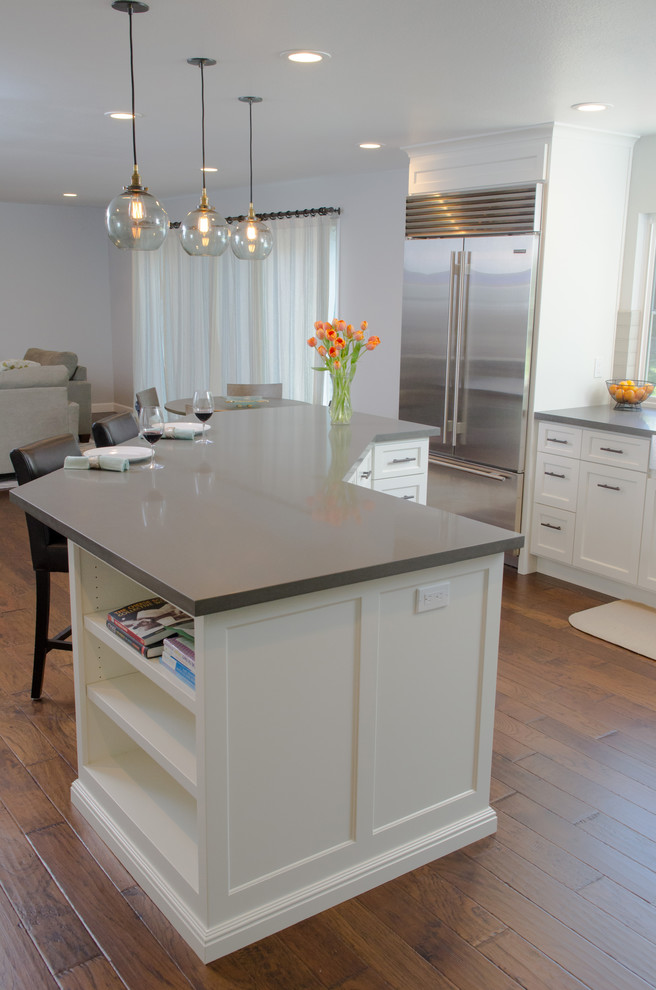 This is an example of a large contemporary l-shaped eat-in kitchen in San Francisco with a farmhouse sink, shaker cabinets, white cabinets, quartz benchtops, grey splashback, subway tile splashback, stainless steel appliances, dark hardwood floors, with island, brown floor and grey benchtop.