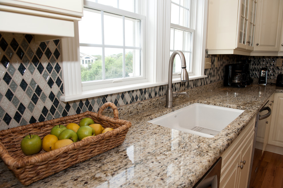 Large transitional light wood floor open concept kitchen photo with an undermount sink, raised-panel cabinets, beige cabinets, granite countertops, multicolored backsplash, mosaic tile backsplash, stainless steel appliances and a peninsula