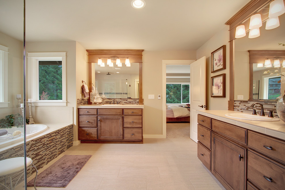 Photo of an arts and crafts master bathroom in Seattle with a drop-in sink, recessed-panel cabinets, medium wood cabinets, tile benchtops, a drop-in tub, a double shower, a two-piece toilet, beige tile, porcelain tile, beige walls and porcelain floors.