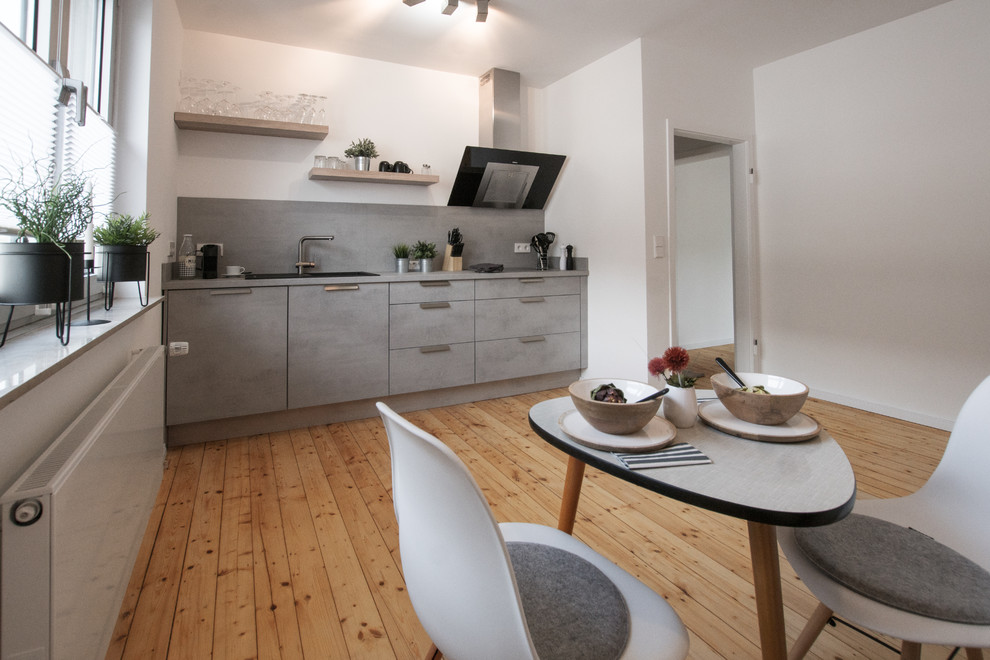 This is an example of a small scandinavian galley eat-in kitchen in Cologne with flat-panel cabinets, grey cabinets, grey splashback, light hardwood floors and grey benchtop.