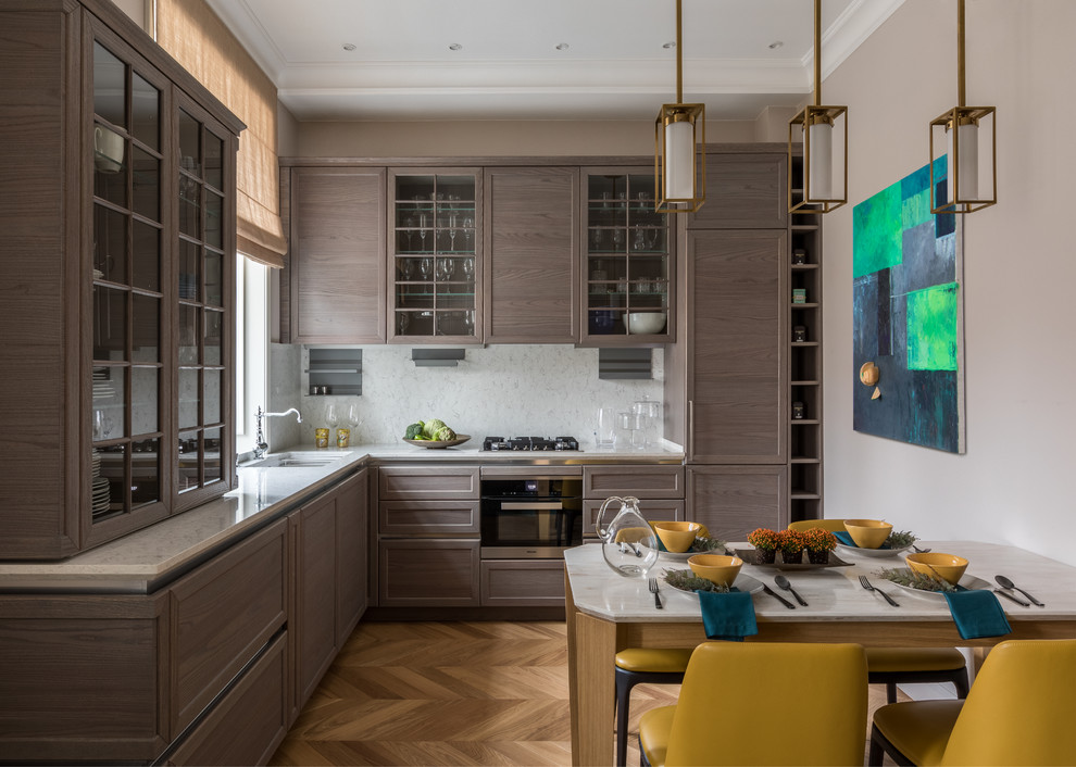 Transitional l-shaped eat-in kitchen in Moscow with an undermount sink, recessed-panel cabinets, medium wood cabinets, white splashback, stainless steel appliances, medium hardwood floors, brown floor, white benchtop and no island.