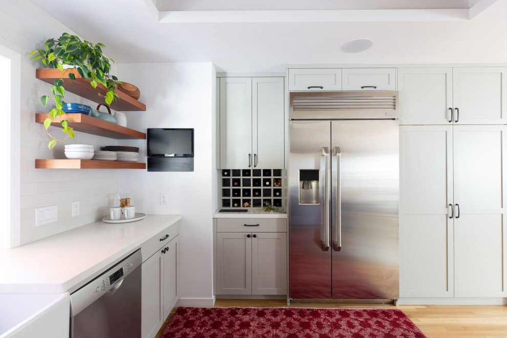 Inspiration for a mid-sized transitional u-shaped light wood floor and brown floor open concept kitchen remodel with a farmhouse sink, shaker cabinets, gray cabinets, quartz countertops, white backsplash, ceramic backsplash, stainless steel appliances, a peninsula and white countertops
