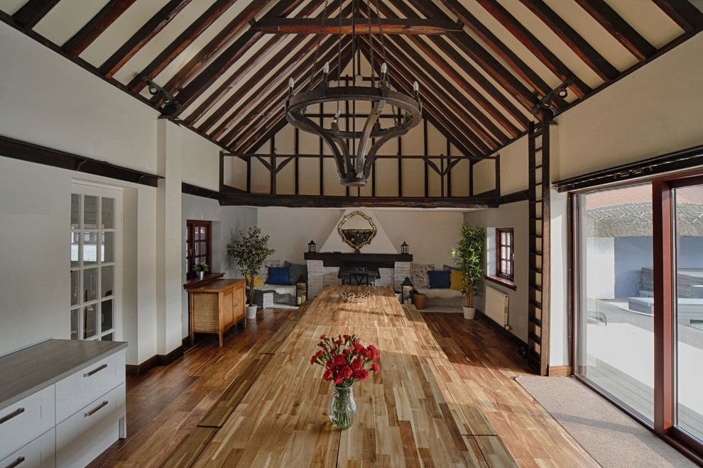 Inspiration for a large country dining room in Other with white walls, dark hardwood floors, a standard fireplace, a brick fireplace surround and brown floor.