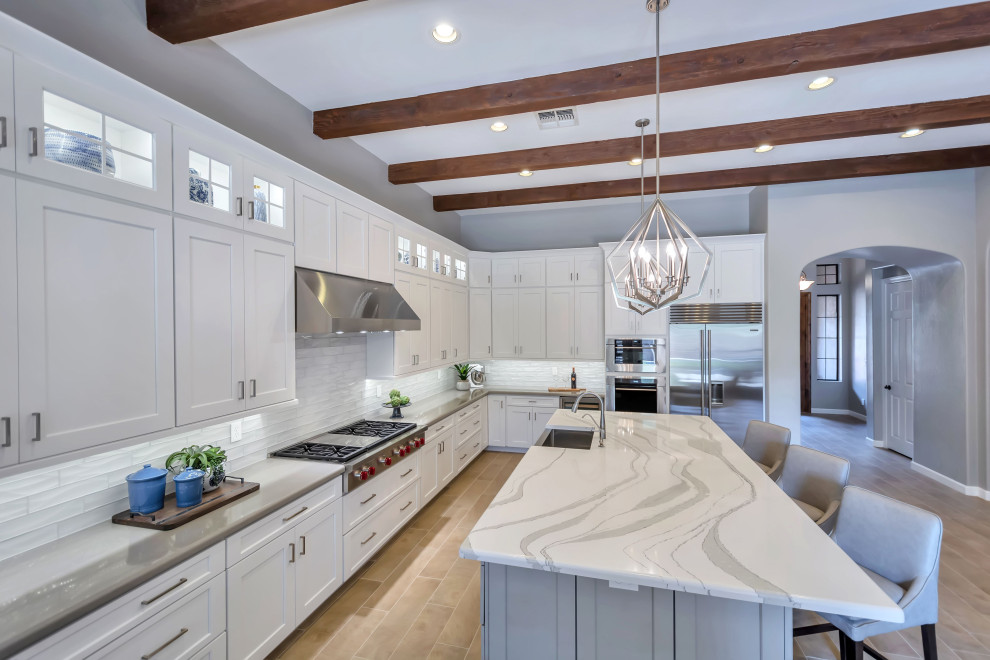 Enclosed kitchen - large transitional u-shaped porcelain tile, beige floor and exposed beam enclosed kitchen idea in Phoenix with a farmhouse sink, shaker cabinets, white cabinets, quartz countertops, white backsplash, glass tile backsplash, stainless steel appliances, an island and white countertops