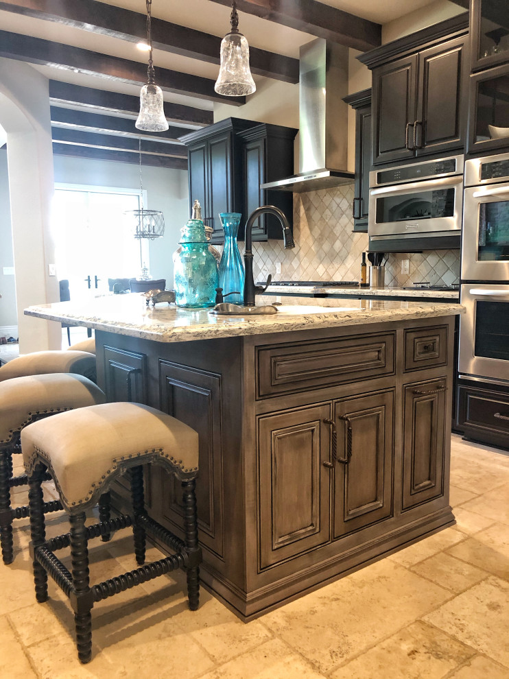 Inspiration for a kitchen in Houston with a double-bowl sink, raised-panel cabinets, distressed cabinets, quartz benchtops, beige splashback, travertine splashback, stainless steel appliances, travertine floors, with island, beige floor, multi-coloured benchtop and exposed beam.