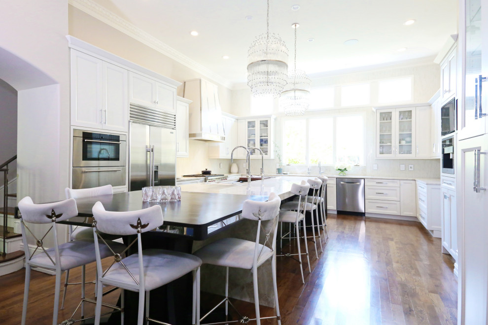 Huge transitional medium tone wood floor and brown floor open concept kitchen photo with an undermount sink, recessed-panel cabinets, white cabinets, quartzite countertops, white backsplash, ceramic backsplash, stainless steel appliances, an island and white countertops
