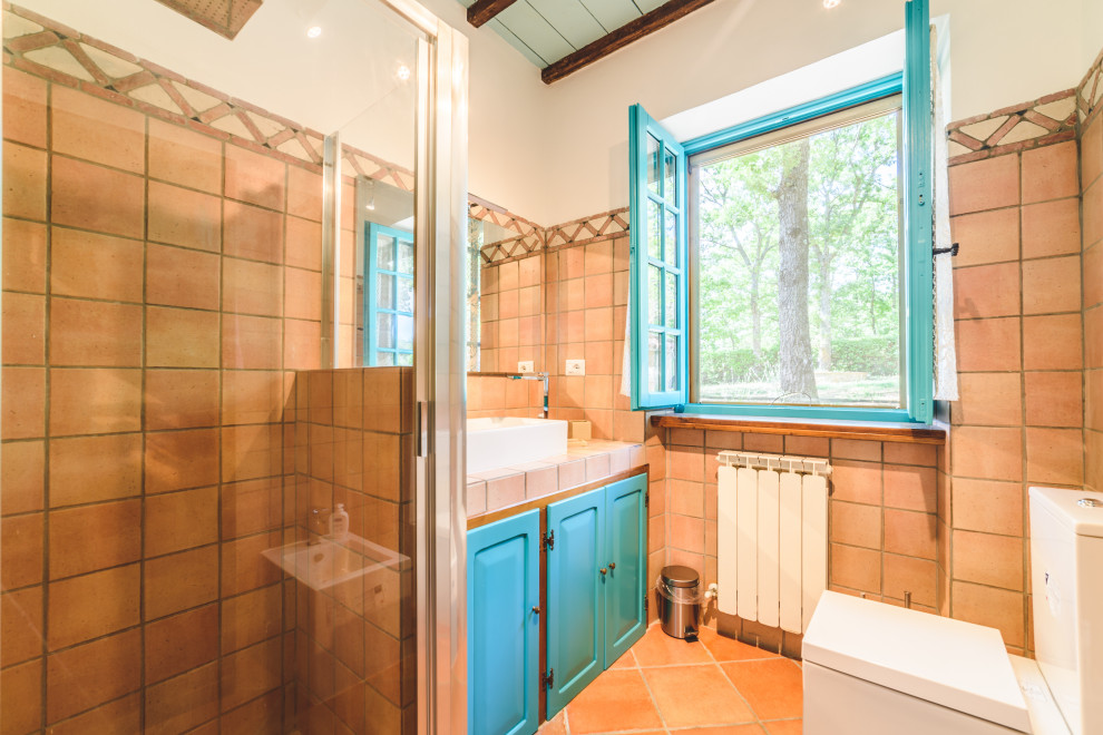 Inspiration for a small modern 3/4 bathroom in Other with louvered cabinets, turquoise cabinets, a corner shower, a one-piece toilet, pink tile, ceramic tile, pink walls, terra-cotta floors, a vessel sink, limestone benchtops, orange floor, a hinged shower door and pink benchtops.