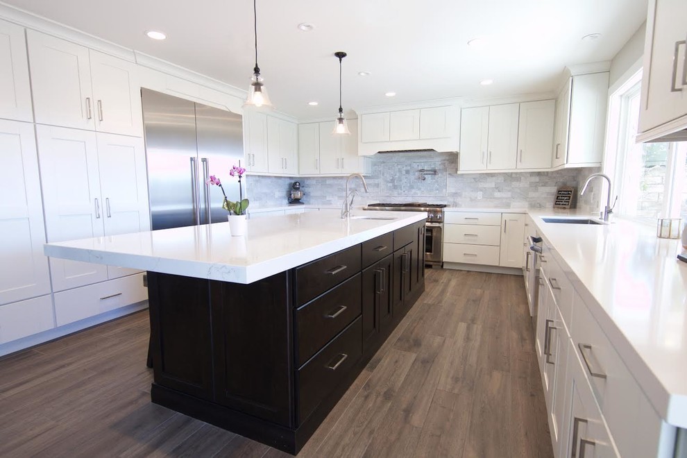 Large contemporary u-shaped open plan kitchen in Orange County with an undermount sink, shaker cabinets, white cabinets, marble benchtops, grey splashback, marble splashback, stainless steel appliances, medium hardwood floors, with island and brown floor.
