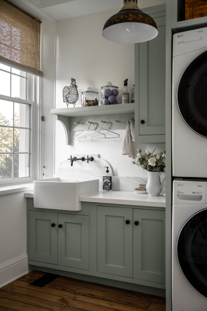 Inspiration for a small single-wall separated utility room in Toronto with a belfast sink, marble worktops, white splashback, marble splashback, white walls, a stacked washer and dryer, brown floors, white worktops, shaker cabinets, green cabinets and medium hardwood flooring.