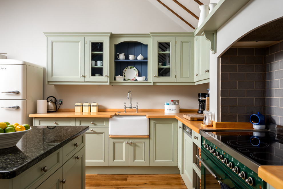 Photo of a large country u-shaped open plan kitchen in Gloucestershire with a farmhouse sink, recessed-panel cabinets, green cabinets, wood benchtops, coloured appliances, medium hardwood floors, with island, brown floor and brown benchtop.