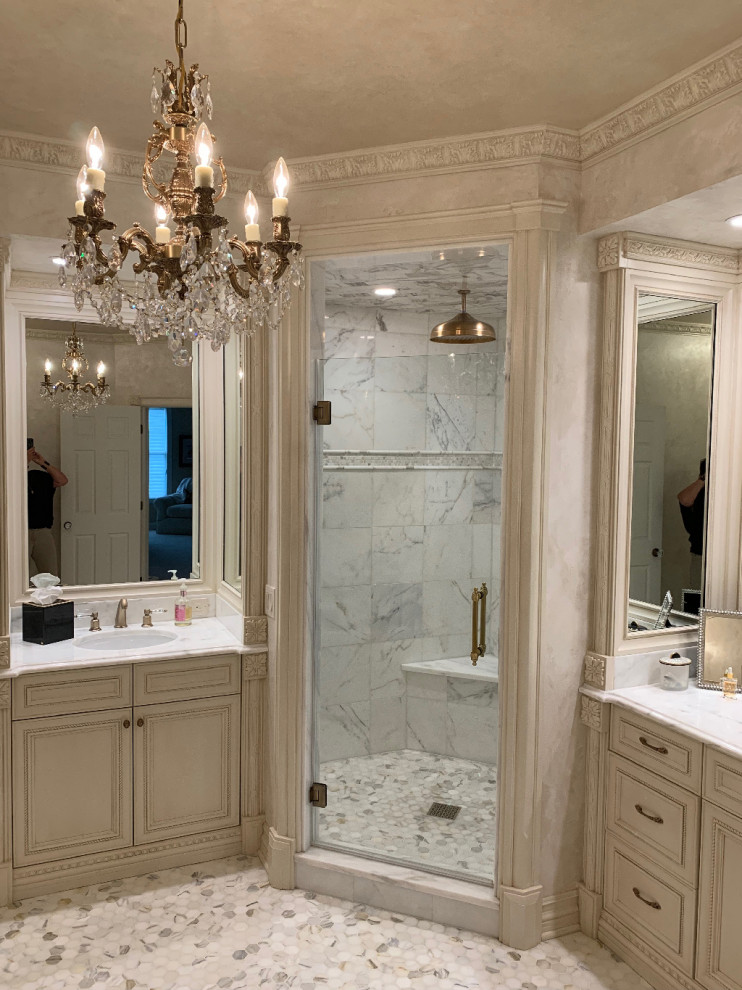 Photo of a large transitional master bathroom in Other with recessed-panel cabinets, beige cabinets, a freestanding tub, a corner shower, beige walls, mosaic tile floors, a drop-in sink, marble benchtops, multi-coloured floor, a hinged shower door and white benchtops.