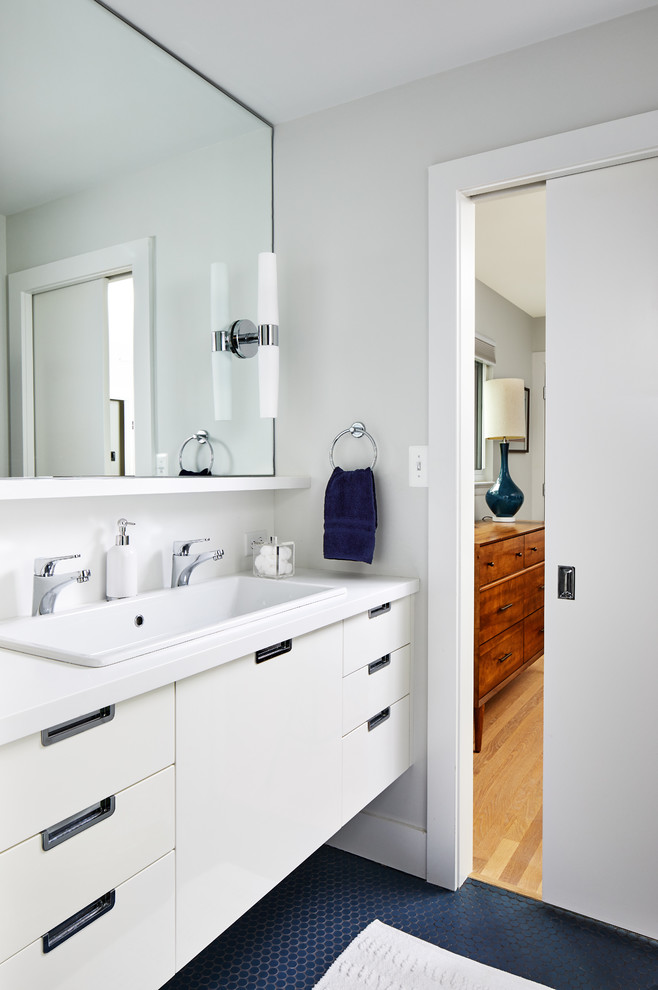 Design ideas for a mid-sized midcentury kids bathroom in DC Metro with flat-panel cabinets, white cabinets, white walls, ceramic floors, a drop-in sink, solid surface benchtops, grey floor and white benchtops.