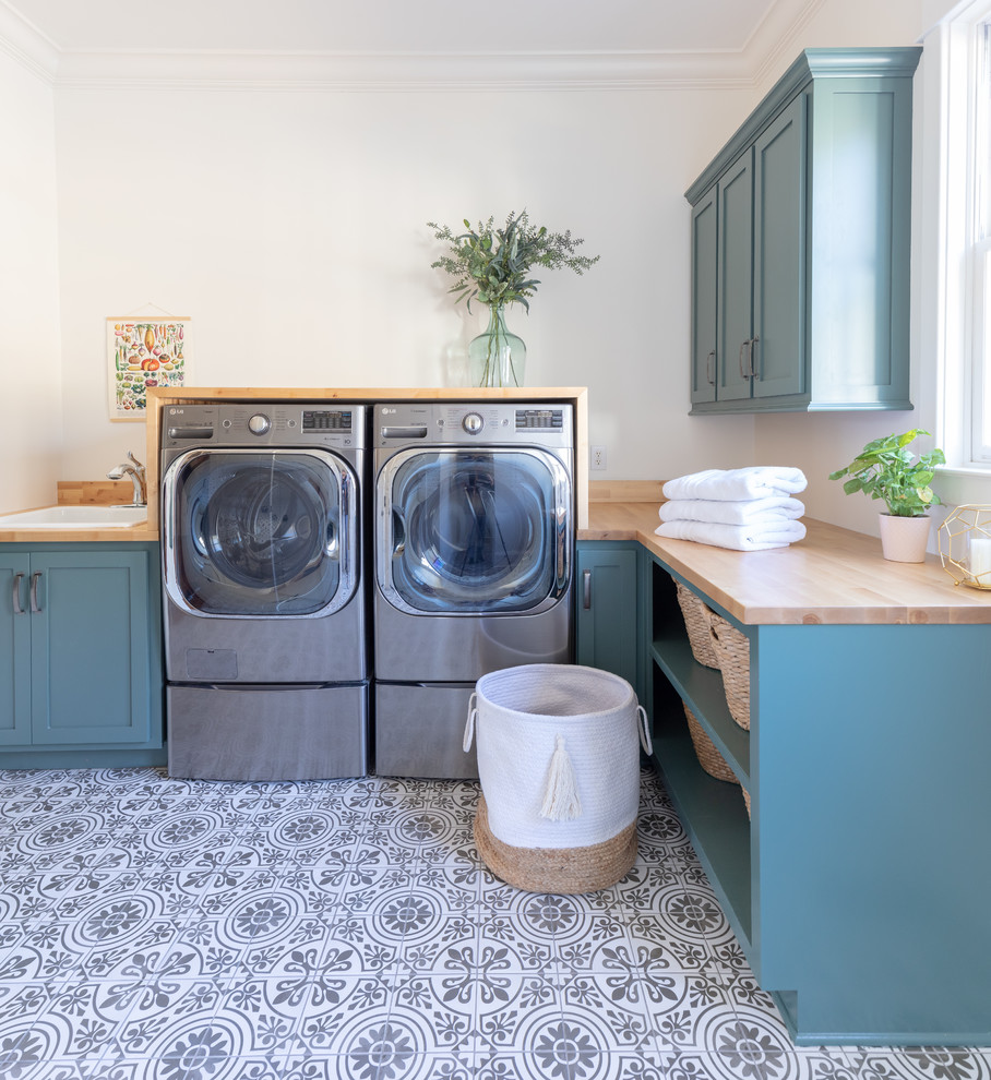 Mid-sized transitional l-shaped dedicated laundry room in Nashville with a drop-in sink, shaker cabinets, green cabinets, wood benchtops, white walls, ceramic floors, a side-by-side washer and dryer, multi-coloured floor and brown benchtop.