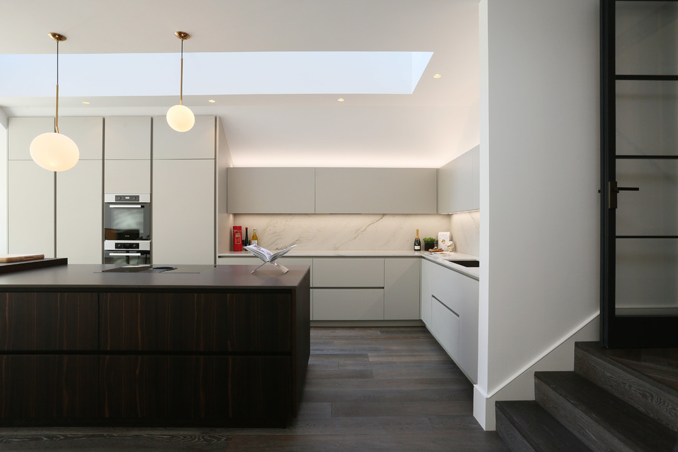 Photo of a mid-sized contemporary l-shaped kitchen in London with an undermount sink, grey cabinets, white splashback, marble splashback, stainless steel appliances, dark hardwood floors, with island, brown floor and white benchtop.
