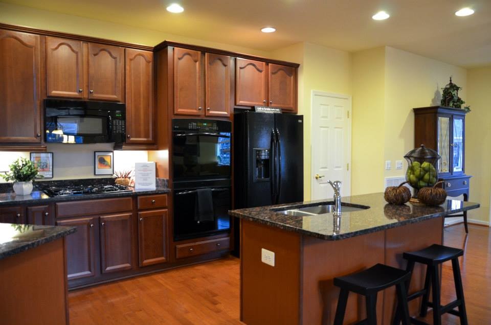 Eat-in kitchen - l-shaped medium tone wood floor eat-in kitchen idea with dark wood cabinets, granite countertops, beige backsplash, black appliances and an island