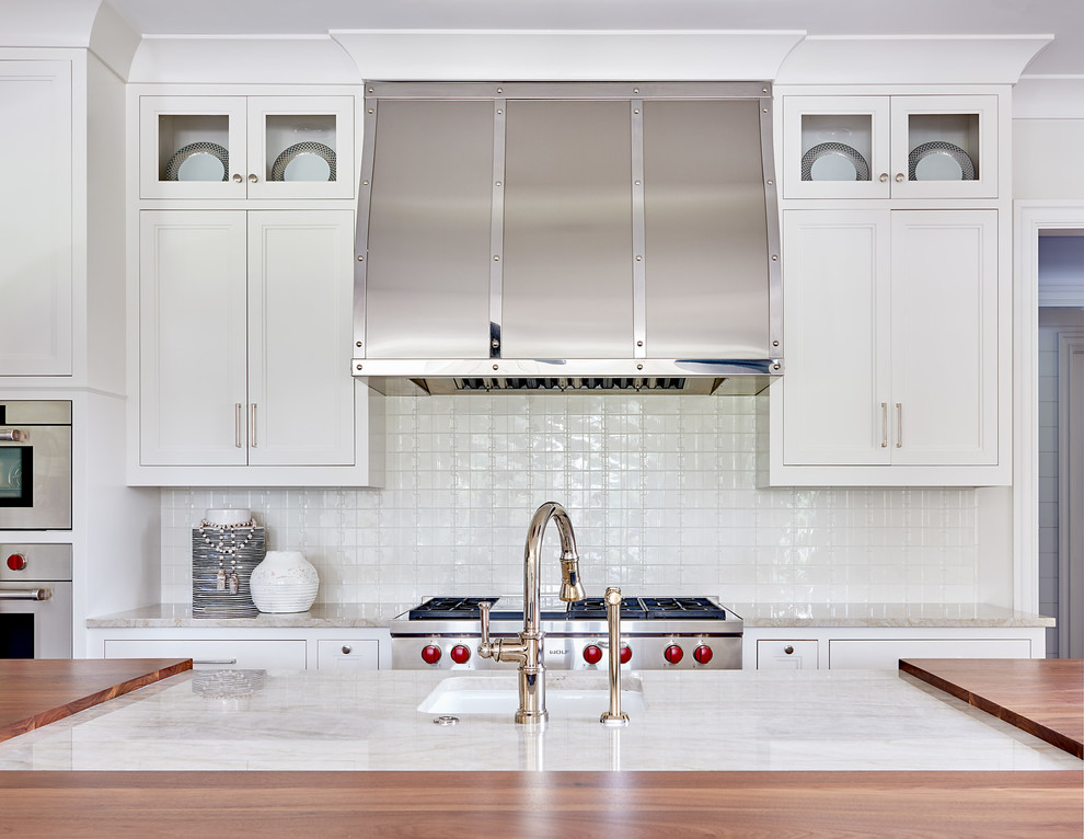 Photo of a large transitional l-shaped eat-in kitchen in Charlotte with a farmhouse sink, raised-panel cabinets, white cabinets, marble benchtops, white splashback, subway tile splashback, stainless steel appliances, dark hardwood floors, with island and brown floor.