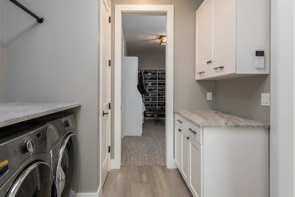Inspiration for a mid-sized country galley dedicated laundry room in Other with shaker cabinets, white cabinets, marble benchtops, a side-by-side washer and dryer, grey benchtop, grey walls, light hardwood floors and beige floor.