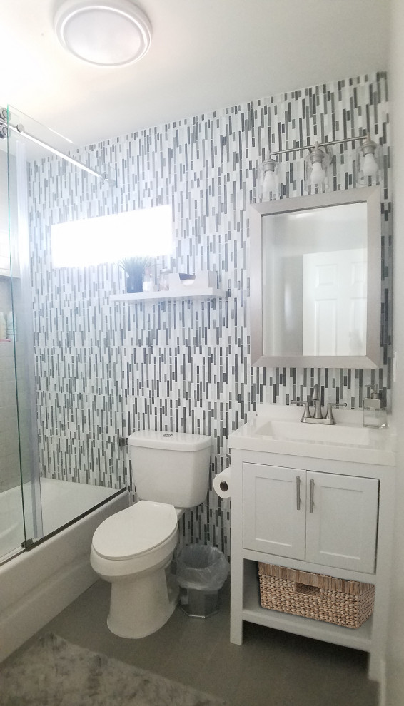 Mid-sized beach style kids bathroom in Los Angeles with recessed-panel cabinets, white cabinets, a freestanding tub, a shower/bathtub combo, a two-piece toilet, gray tile, mosaic tile, beige walls, porcelain floors, an integrated sink, marble benchtops, grey floor, a sliding shower screen, white benchtops, a single vanity and a freestanding vanity.