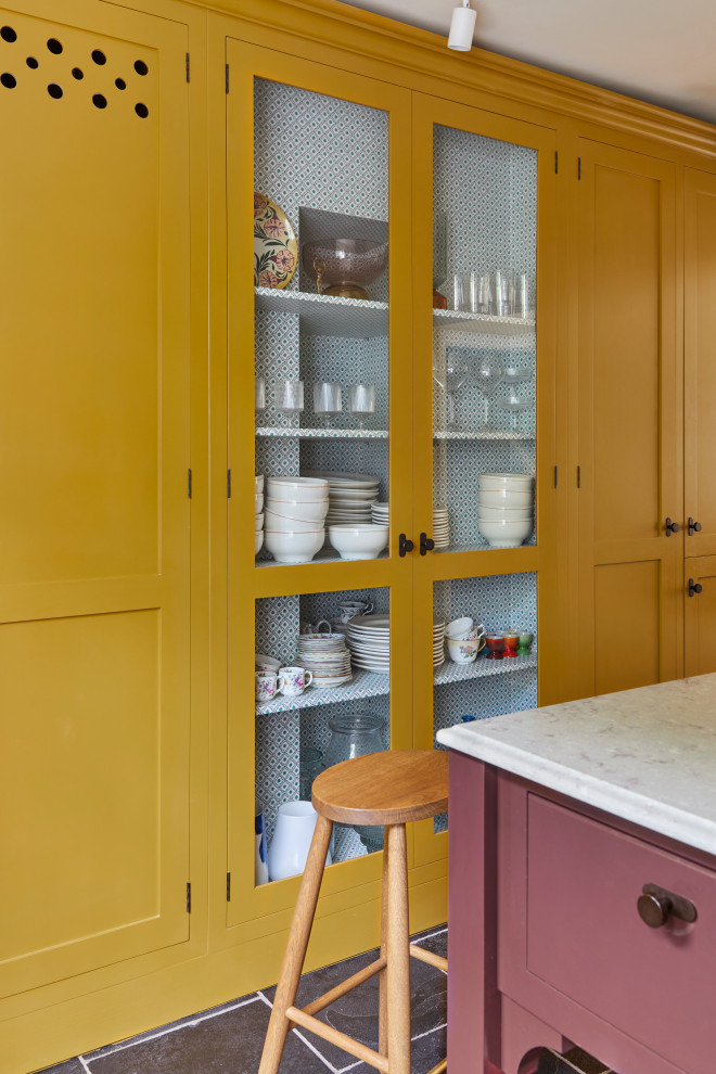 Design ideas for a large transitional eat-in kitchen in London with a farmhouse sink, shaker cabinets, yellow cabinets, marble benchtops, white splashback, ceramic splashback, white appliances, limestone floors, with island, black floor and brown benchtop.