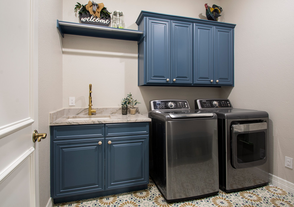 Design ideas for a mid-sized transitional galley utility room in Dallas with an undermount sink, raised-panel cabinets, blue cabinets, quartzite benchtops, grey walls, porcelain floors, a side-by-side washer and dryer, multi-coloured floor and beige benchtop.