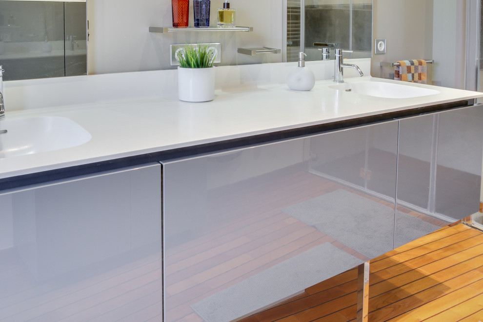 Idées déco pour une salle de bain principale contemporaine de taille moyenne avec un placard à porte plane, des portes de placard grises, une douche à l'italienne, un carrelage gris, des carreaux de céramique, un mur gris, parquet clair, un lavabo intégré, une cabine de douche à porte battante et un plan de toilette blanc.