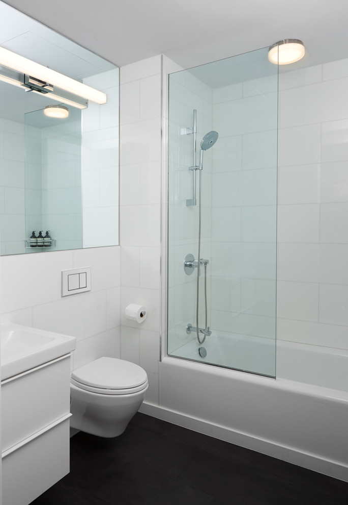 Design ideas for a mid-sized contemporary master bathroom in New York with flat-panel cabinets, white cabinets, an alcove tub, a shower/bathtub combo, a wall-mount toilet, white tile, glass tile, white walls, porcelain floors, an integrated sink, black floor and an open shower.