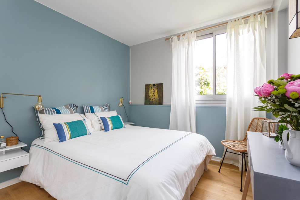 This is an example of a beach style master bedroom in Paris with blue walls, light hardwood floors and no fireplace.