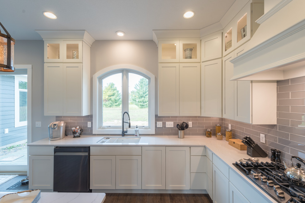 Country l-shaped kitchen/diner in Minneapolis with a submerged sink, shaker cabinets, white cabinets, engineered stone countertops, grey splashback, metro tiled splashback, stainless steel appliances, medium hardwood flooring, an island and white worktops.