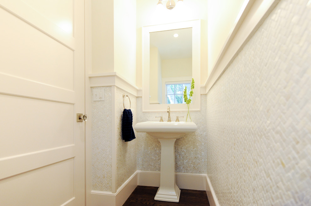 This is an example of a beach style powder room in Boston with a two-piece toilet, beige tile, beige walls, medium hardwood floors, a pedestal sink and brown floor.