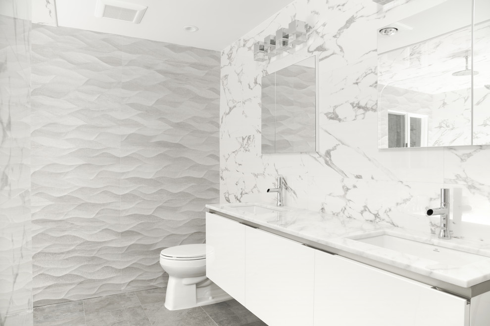 Inspiration for a large midcentury master bathroom in New York with flat-panel cabinets, grey cabinets, a drop-in tub, a curbless shower, a one-piece toilet, gray tile, porcelain tile, grey walls, porcelain floors, an undermount sink, marble benchtops, grey floor and an open shower.