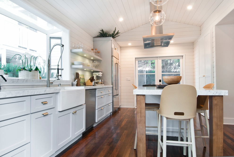 Inspiration for a mid-sized country galley eat-in kitchen in Los Angeles with a farmhouse sink, shaker cabinets, white cabinets, marble benchtops, white splashback, timber splashback, stainless steel appliances, painted wood floors and with island.