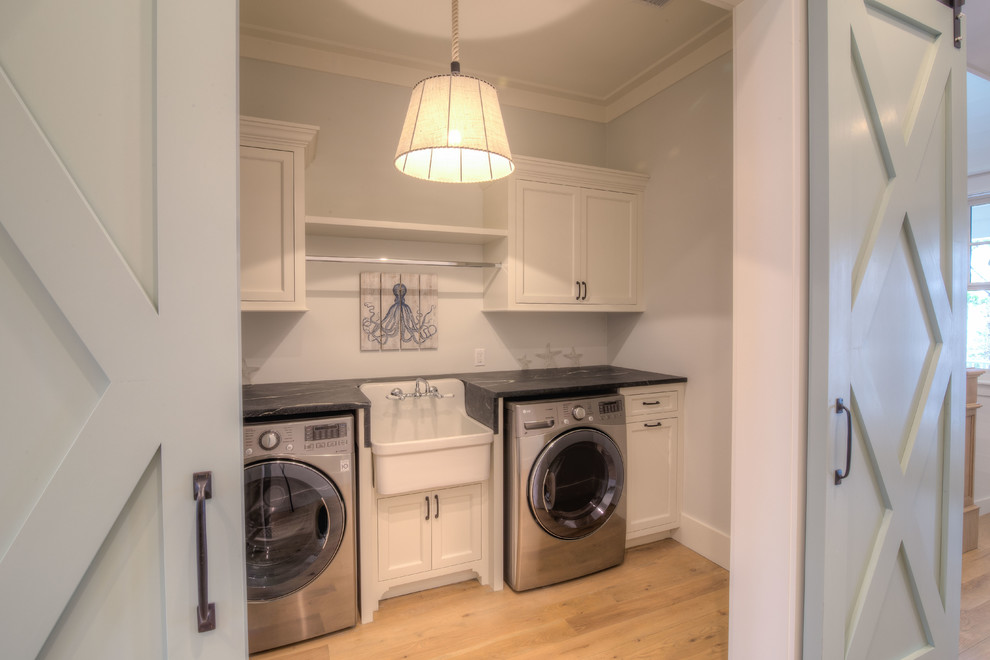 Photo of an expansive beach style single-wall dedicated laundry room in Atlanta with an utility sink, recessed-panel cabinets, white cabinets, soapstone benchtops, grey walls, light hardwood floors, a side-by-side washer and dryer and beige floor.