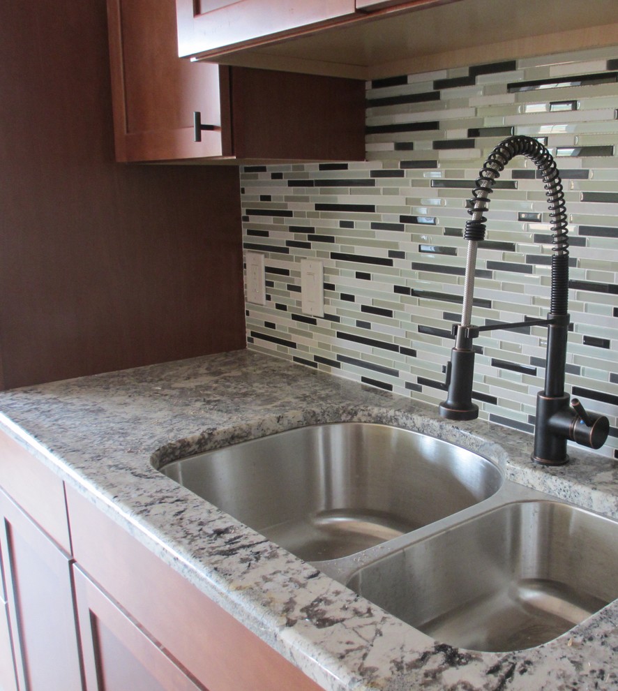 Example of a transitional kitchen design with a double-bowl sink, shaker cabinets, medium tone wood cabinets, quartzite countertops, gray backsplash, glass tile backsplash and stainless steel appliances