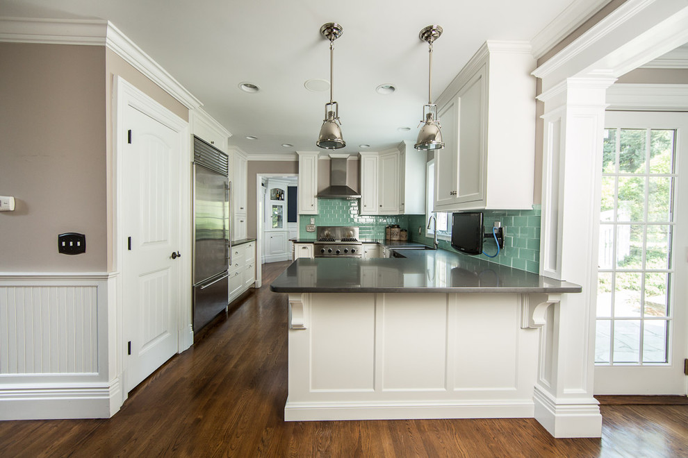 Inspiration for a mid-sized transitional kitchen in New York with a farmhouse sink, shaker cabinets, white cabinets, green splashback, subway tile splashback, stainless steel appliances, medium hardwood floors, a peninsula and brown floor.