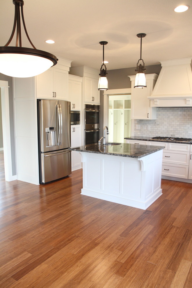 This is an example of a country u-shaped eat-in kitchen in Minneapolis with an undermount sink, shaker cabinets, white cabinets, granite benchtops, white splashback, subway tile splashback and stainless steel appliances.