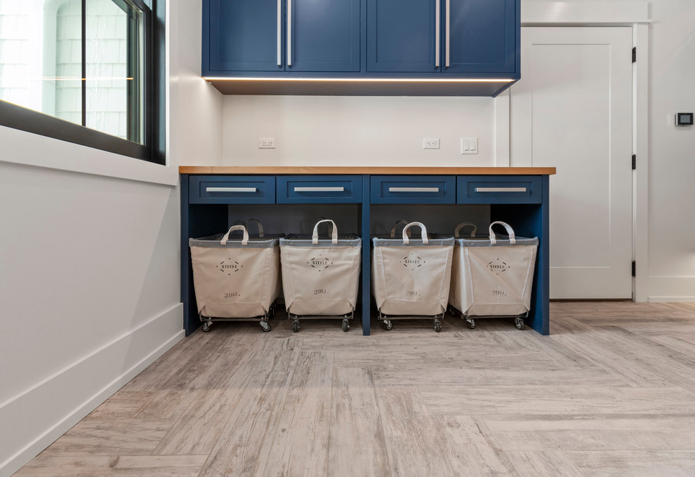 Design ideas for a mid-sized contemporary single-wall dedicated laundry room in Other with an undermount sink, shaker cabinets, blue cabinets, wood benchtops, white walls, light hardwood floors, a side-by-side washer and dryer, beige floor and blue benchtop.