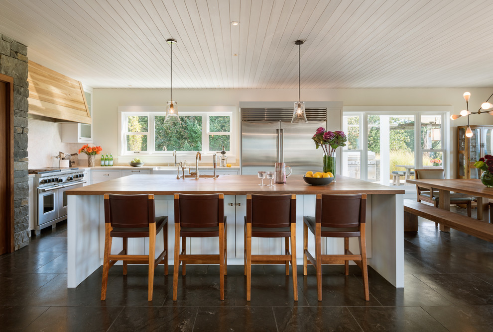 This is an example of a large country single-wall open plan kitchen in Other with an undermount sink, louvered cabinets, white cabinets, wood benchtops, stainless steel appliances, slate floors, with island and brown floor.