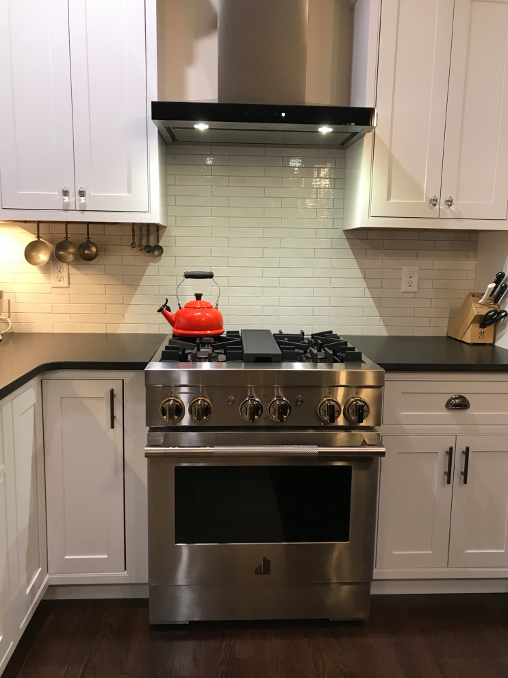 Example of a mid-sized transitional l-shaped laminate floor and brown floor eat-in kitchen design with a farmhouse sink, beaded inset cabinets, white cabinets, quartz countertops, white backsplash, subway tile backsplash, stainless steel appliances and an island